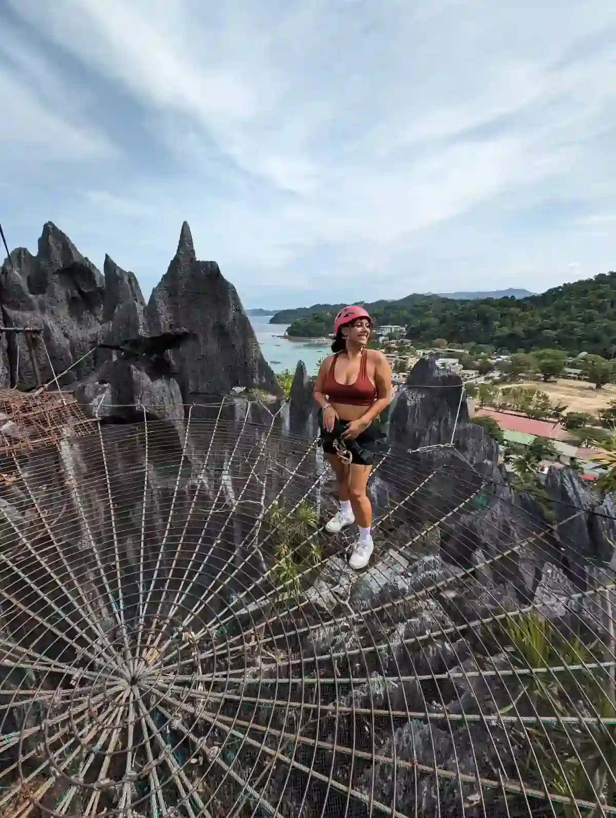 Traveller standing on the spider web net of the El Nido canopy walk above the town and bay