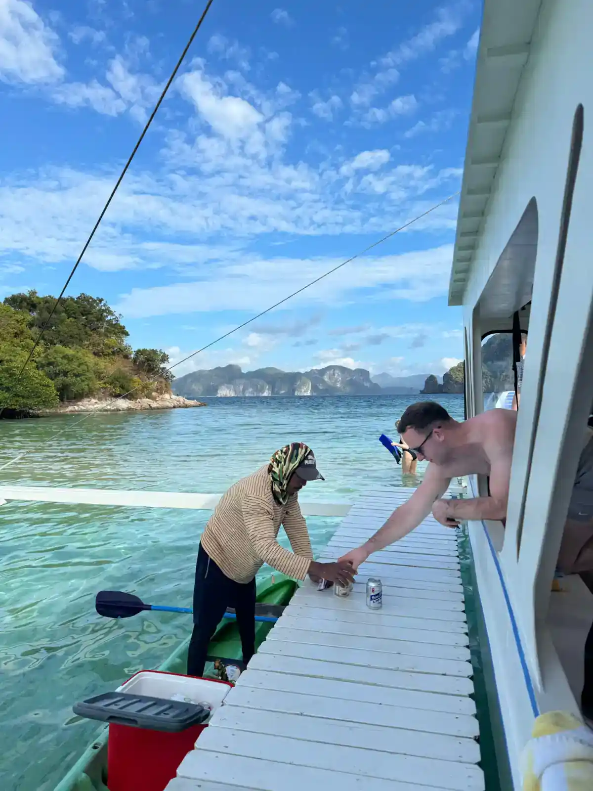 Traveller buying drinks from a local kayak vendor while island hopping in Bacuit Bay, El Nido