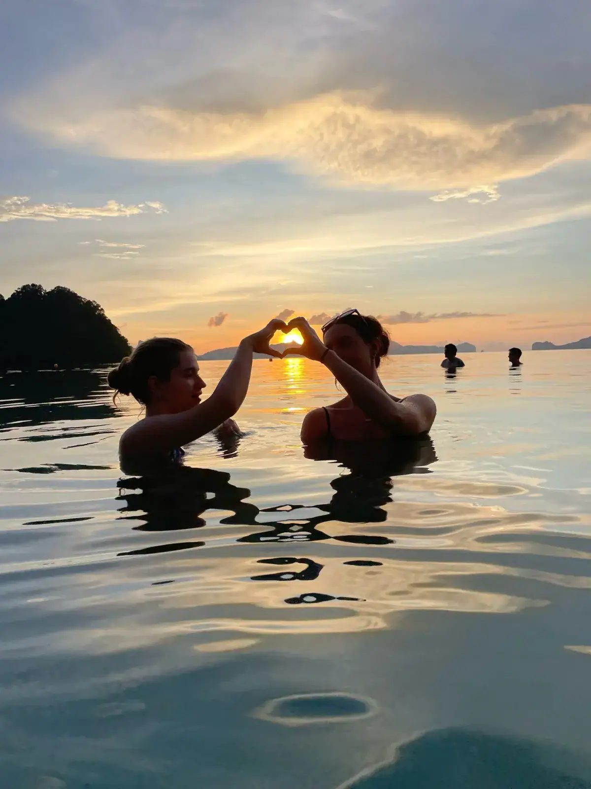 Two friends making a heart shape against the sunset while swimming in El Nido