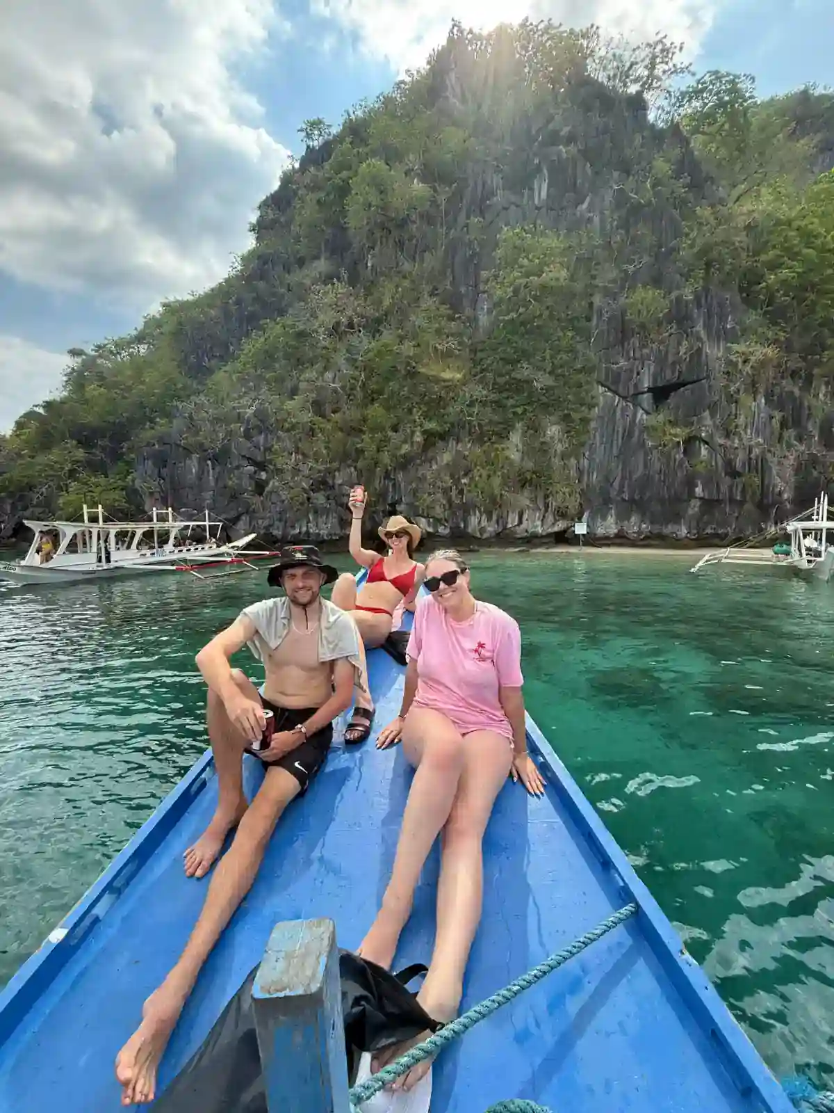 Travellers relaxing on the bow of a bangka boat beside limestone cliffs while island hopping in El Nido